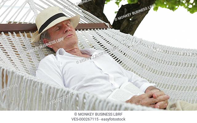Senior man wearing straw hat resting in hammock.Shot on Canon 5d Mk2 with a frame rate of 30fps