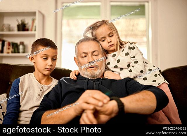 Grandfather using smart watch sitting with grandchildren at home