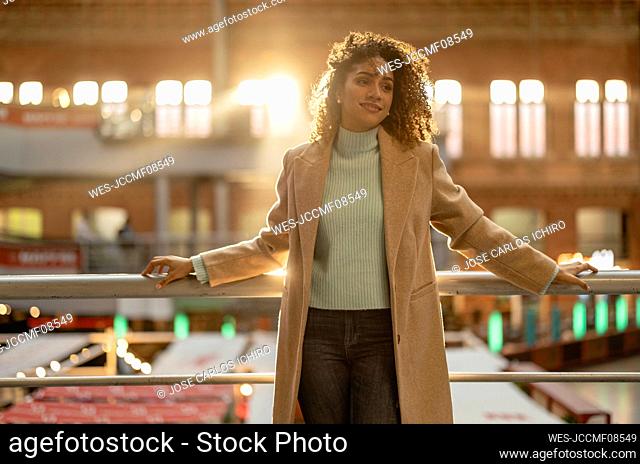 Smiling woman with curly hair leaning on railing at station