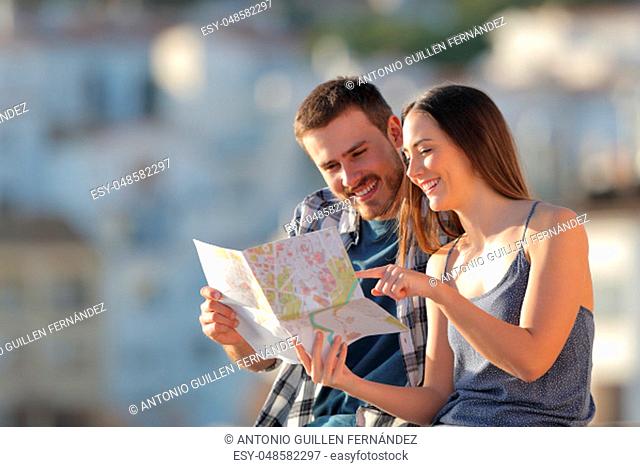 Couple of happy tourists checking paper guide in a town on vacation