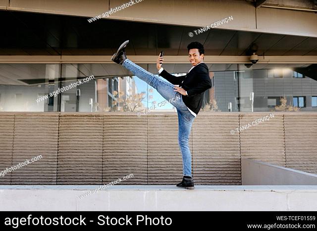 Flexible businessman with smart phone standing on one leg