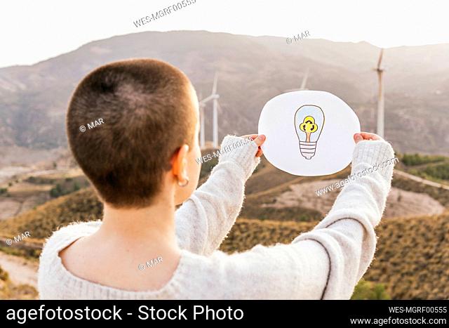 Woman holding light bulb drawing paper at wind farm