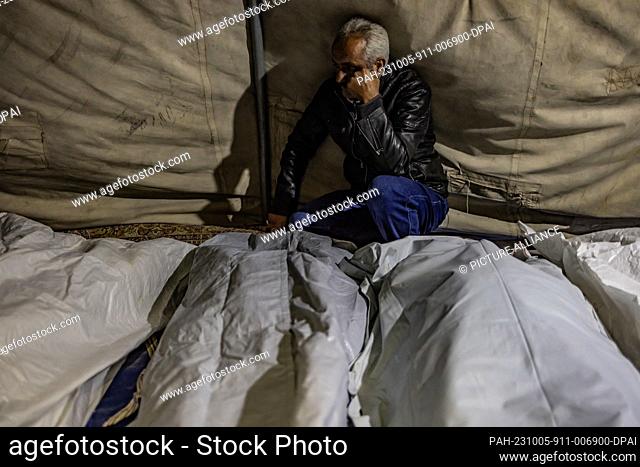05 October 2023, Syria, Aleppo: A man sits near the bodies of his relatives who were killed as a result of a missile strike targeting their house in the town of...