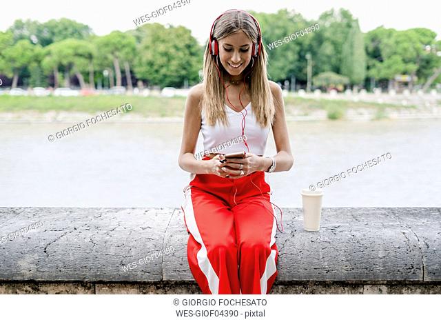Smiling teenage girl wearing headphones and using cell phone at the riverside
