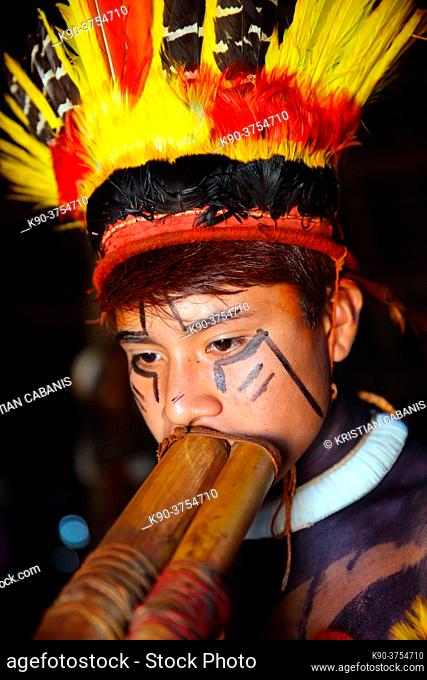 Portrait of young indio tribes man in festive costume and feathers in his hair plaing his long pipe, Mato Grosso, Brazil, South America