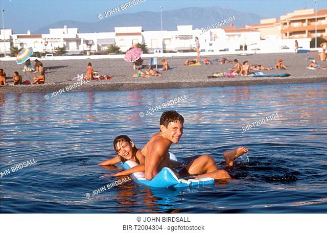 Young children playing on lilo in sea at Salobrena, Andalucia, with the beach and town in background