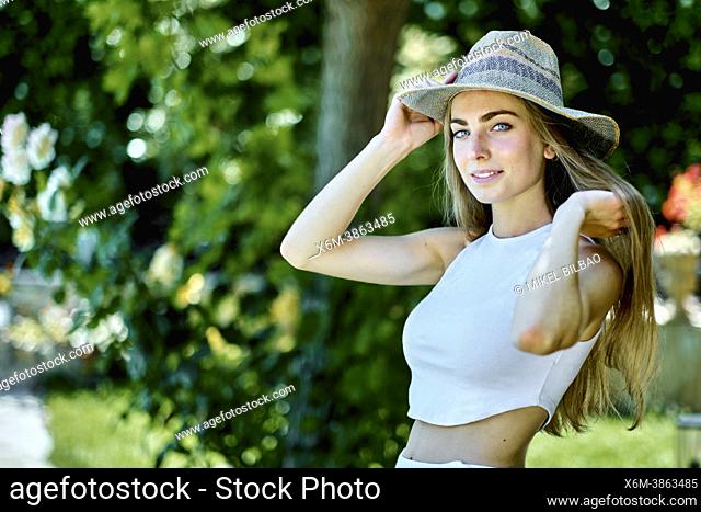 Portrait of a young beautiful caucasian woman in her 20's with long hair and blue eyes wearing a hat outdoor in a garden. Lifestyle concept