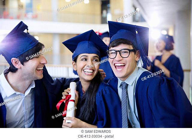 Happy college graduates in cap and gown celebrating with diploma