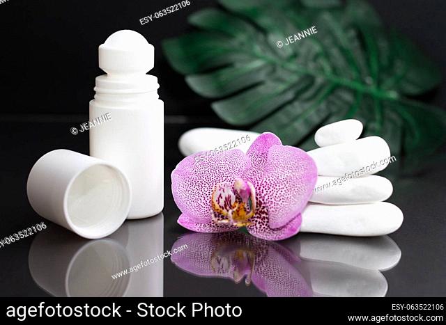 Beautiful lilac orchid flower and white roll-on deodorant with white stones and monstera leaves, on black background
