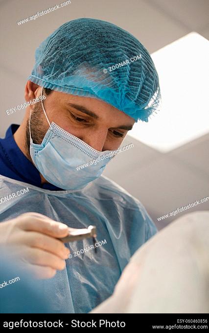 Doctor with drill in hand looking at a patient in stomatology room, close up
