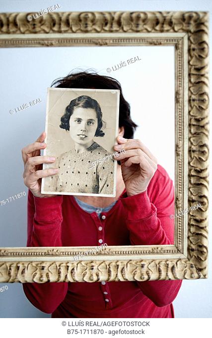 Mujer joven dentro de un marco dorado con retrato antiguo en las manos tapandole la cara, Young woman in a gold frame with old picture in her hands covering her...
