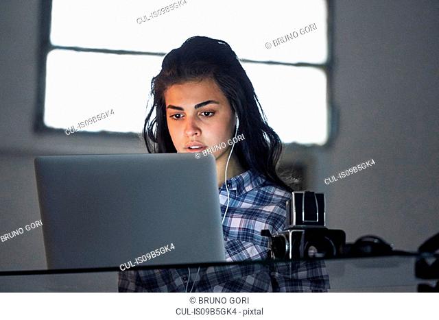 Woman wearing ear phones and working on laptop