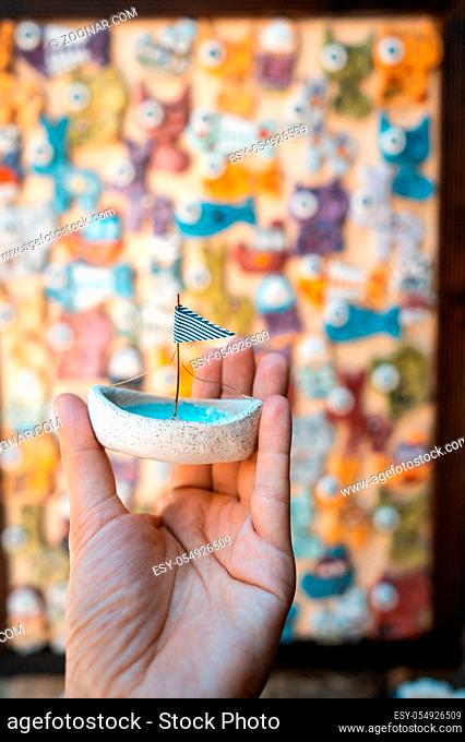 Man's hand holds a toy sailboat with a blue flag. In the background, you can see a wall with colorful animals and fish