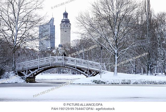 29 January 2019, Saxony, Leipzig: A man stands on a bridge in winterly Johannapark. In the background the tower of the New Town Hall and the striking City Tower