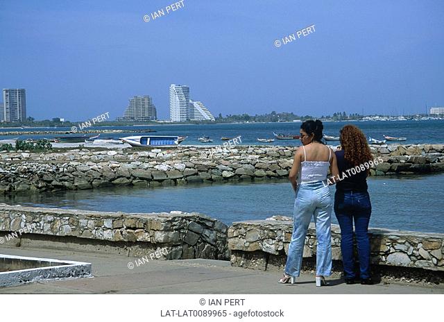 Belle Vista Beach. Two women standing by sea wall. Jetty. Boat. View of tall buildings