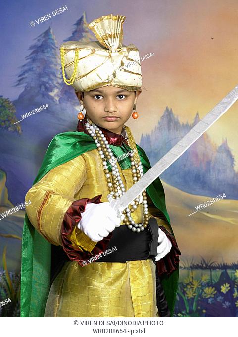 South Asian Indian boy dressed as prince holding sword performing fancy dress competition on stage in nursery school MR