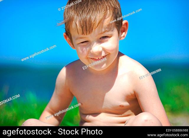 Happy child is sitting on the beach on a Sunny day. White Caucasian boy is sunbathing in the sun