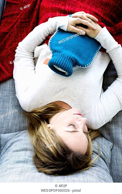 Germany, Bavaria, Munich, Young woman sleeping on couch with hot water bottle