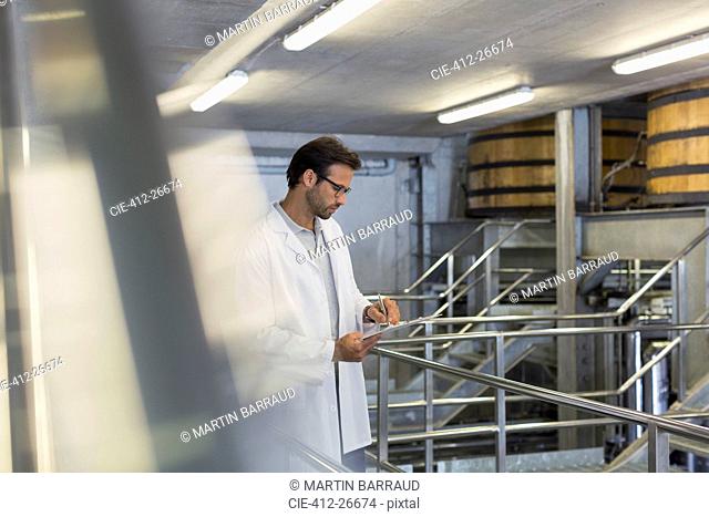 Vintner in lab coat with clipboard in winery cellar