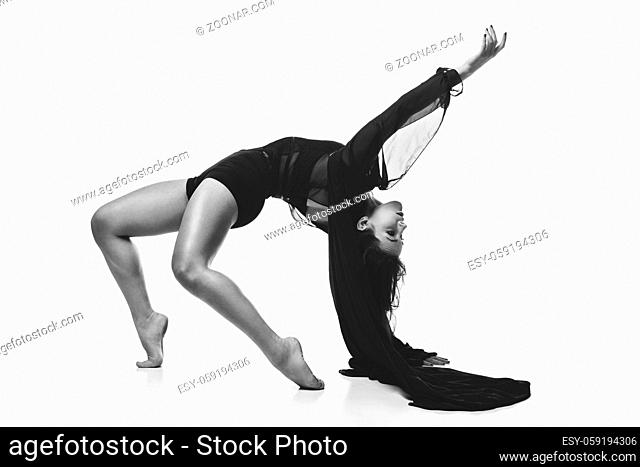 Beautiful modern dancer young woman in black flyings fabrics making dance moves. Isolated on white background. Copy space. Monochrome