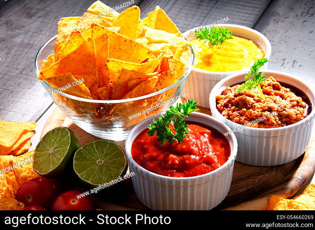 Composition with glass bowl of tortilla chips and dipping sauces