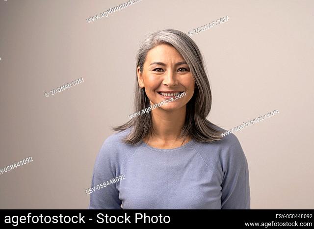 Charming Middle-Aged Asian Woman Broadly Smiles At Camera. Horizontal Studio Shot Of Graceful Smiling Woman. Portrait