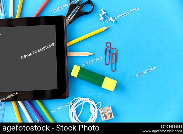 tablet pc and school supplies on blue background