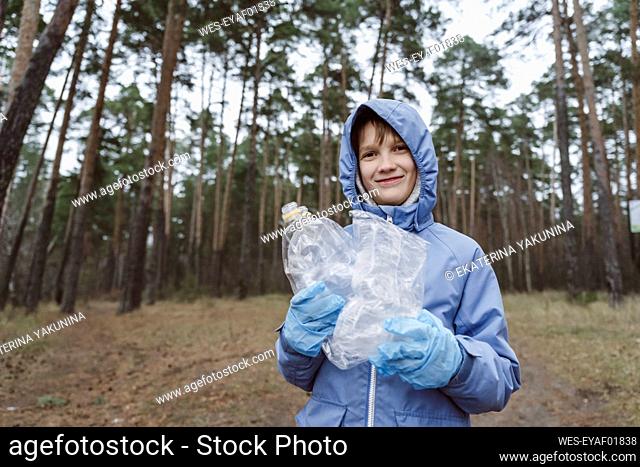 Niño sonriente sosteniendo desechos plásticos en el bosque