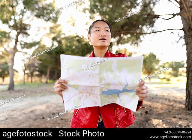 Young woman holding map looking away in forest
