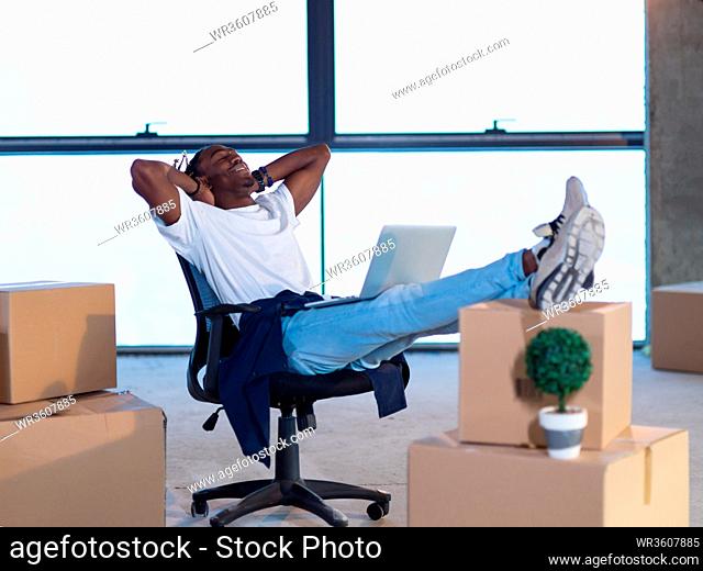 young african american male architect taking a break on construction site while checking documents and business workflow with cardboard boxes around him in new...