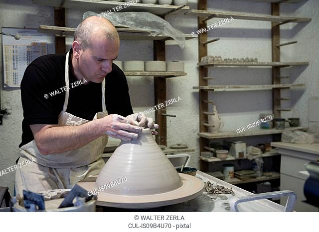Male potter shaping clay pot on pottery wheel in workshop