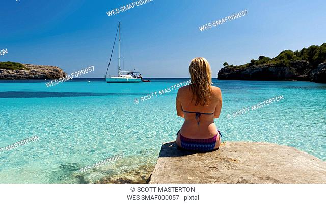 Spain, Menorca, Woman sitting on jetty at Cala Turqueta
