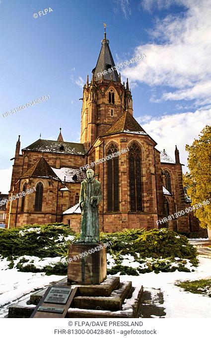 Statue of Benedictine monk and Roman Catholic church in snow, St. Peter and St. Paul's Church, Wissembourg, Bas-Rhin, Alsace, France, December