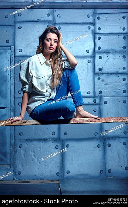 Portrait of young beautiful blonde woman is sitting on a board. Female on metal wall background