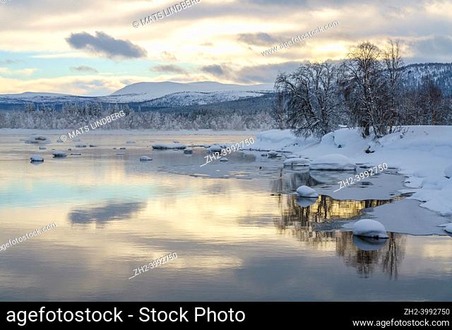 Winter landscape with river, sky reflecting in the water, nice warm colors, mountain in background, Tjåmmotis, Swedish Lapland, Sweden