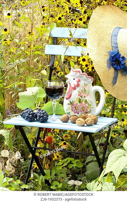 Summer arrangements in the garden includes blue painted chair, glass of domestic Slovenian vine, grapes, straw hat, walnuts and pitcher
