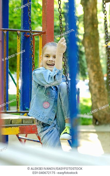 The girl joyfully and fervently laughs sitting on a hanging ladder in the playground