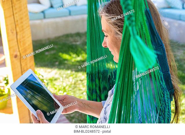 Older Caucasian woman reading digital tablet in green hammock