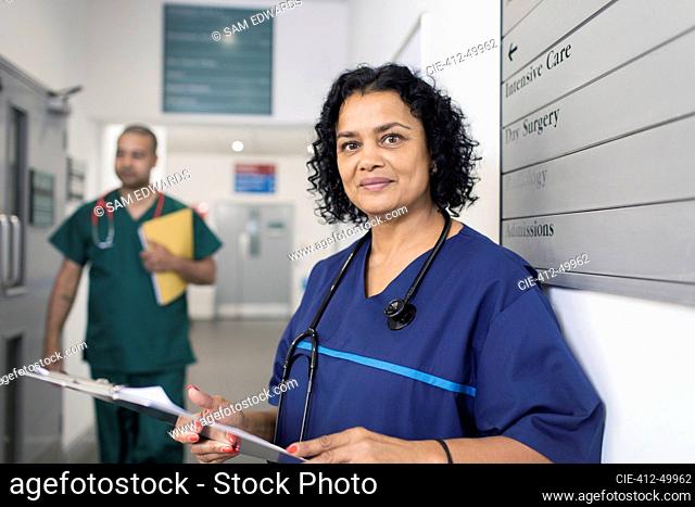 Portrait confident female doctor with medical chart, making rounds in hospital corridor