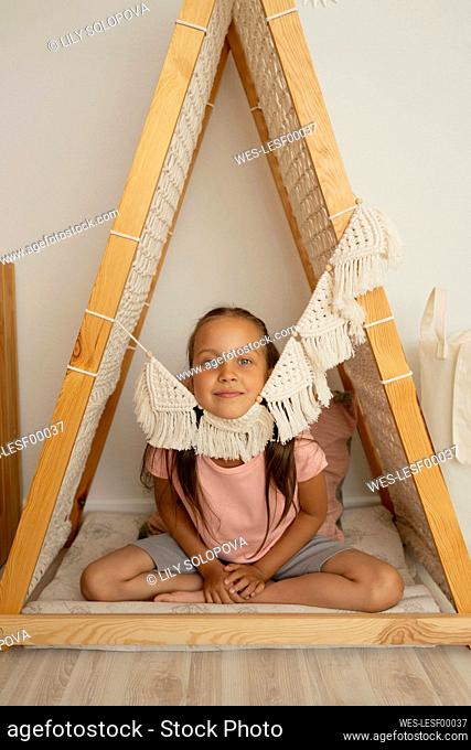 Smiling cute girl sitting in wooden tent at home