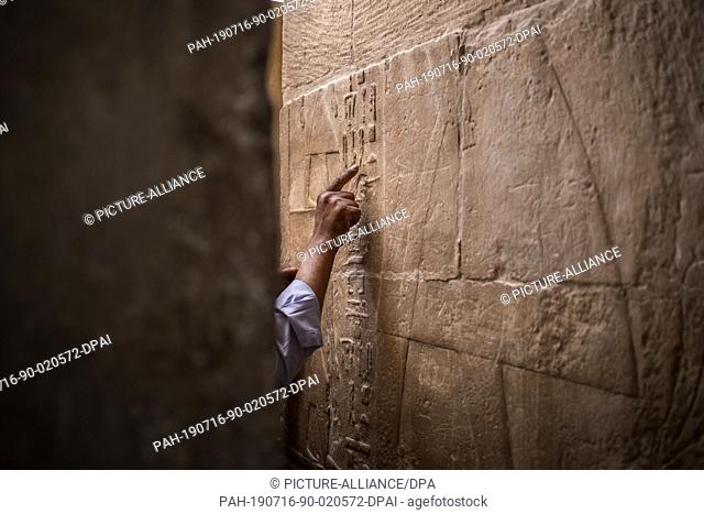 16 July 2019, Egypt, Giza: A Egyptian man points at hieroglyphs in the mastaba tomb of Seshem Nefer Theti at the Giza Pyramid complex