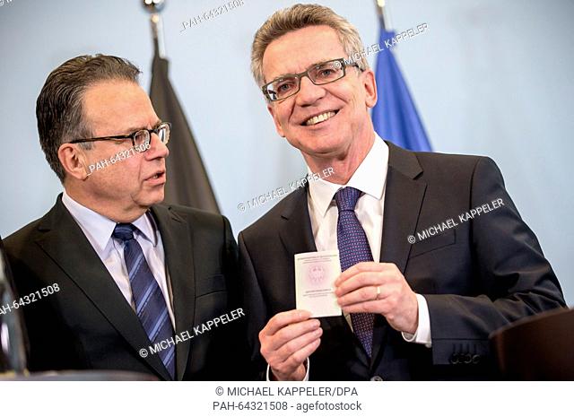 German Interior Minister Thomas de Maiziere (R) holds up the new refugee ID next to the director of the Federal Office for Migration and Refugees