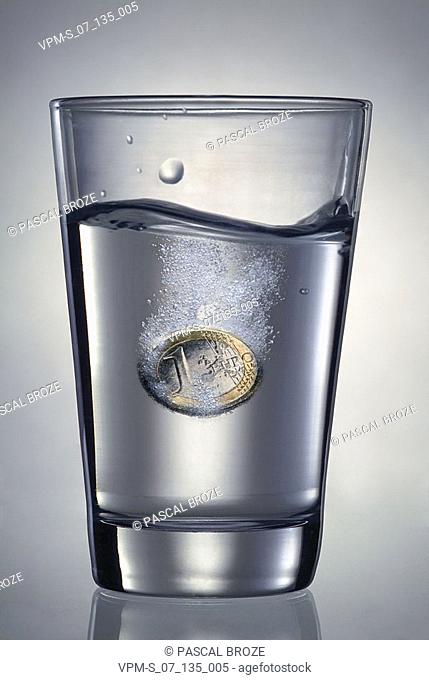 Close-up of one Euro coin dissolving in a glass of water