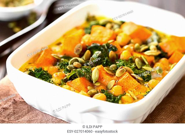 Baked pumpkin, kale and chickpea casserole with pumpkin seeds on top in casserole dish, photographed with natural light (Selective Focus