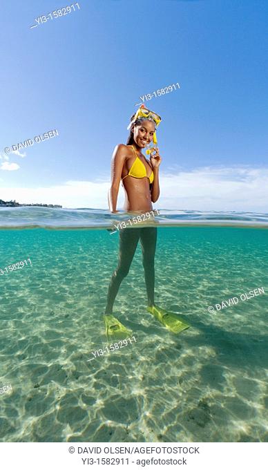 Over and underwater view of smiling girl with snorkel, mask, and fins at Lahaina, Maui, Hawaii