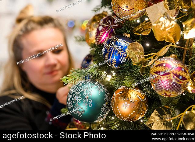 PRODUCTION - 30 November 2023, Thuringia, Lauscha: Liesa-Marie Fehrmann, an employee at Krebs-Glas, places colored Christmas tree baubles from the ""Jewels""...