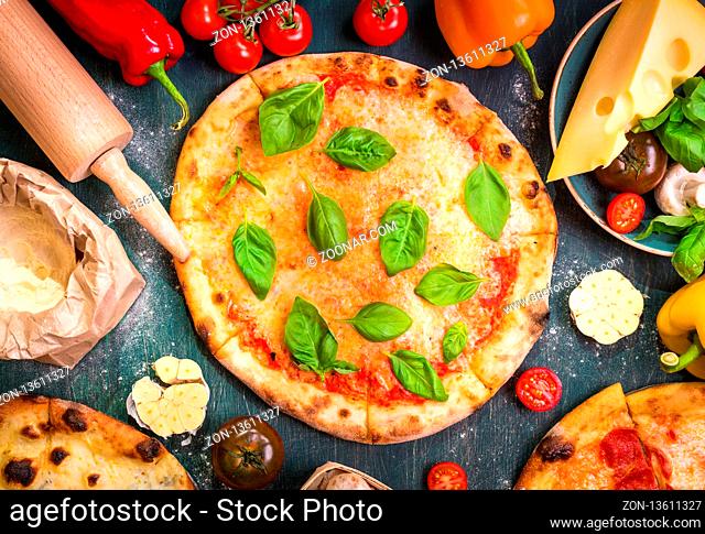 Delicious baked pizza and ingredients for making pizza. Flour, cheese, tomatoes, basil, pepperoni, mushrooms and rolling pin over wooden background