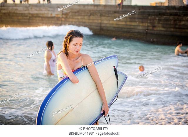 Amputado de raza mixta llevando tablas de surf en la playa