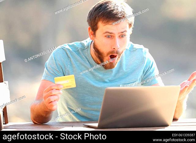 Amazed man buying online with a laptop and credit card in nature