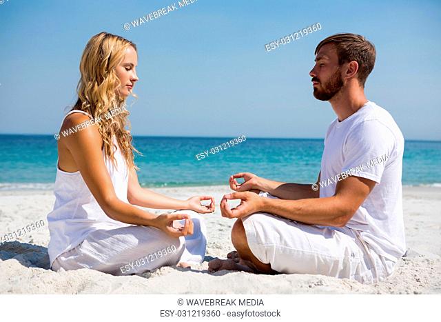 Side view of couple practicing meditation at beach